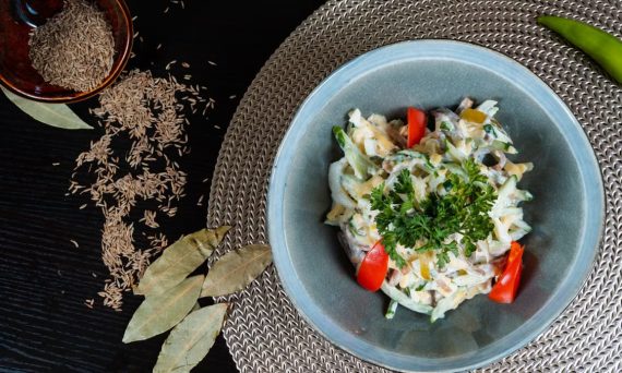 Fresh herb salad with tomatoes, cumin seeds, and spices on a woven mat.